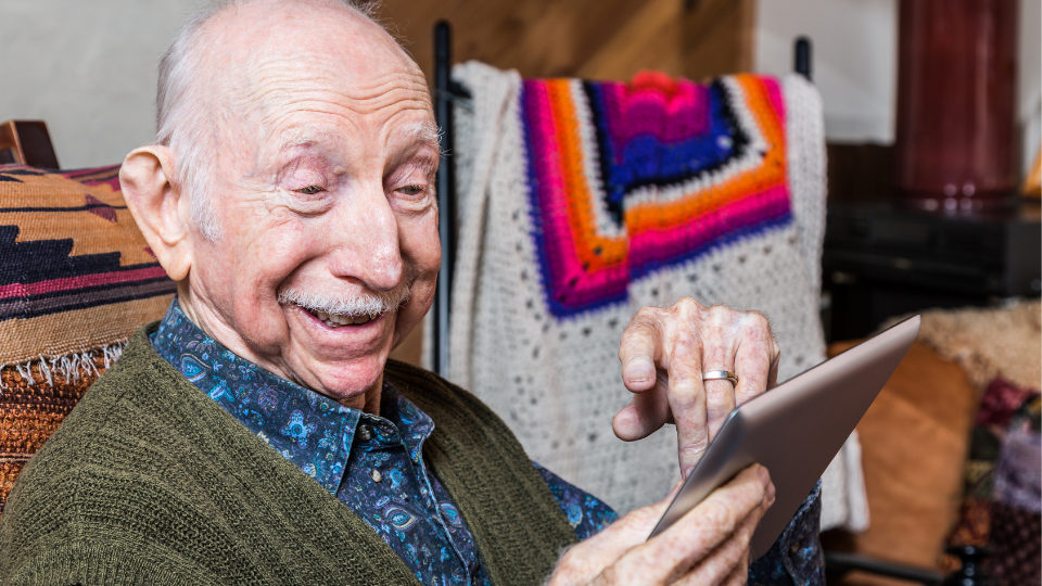 Elderly man on a tablet appearing to be watching/speaking to someone.