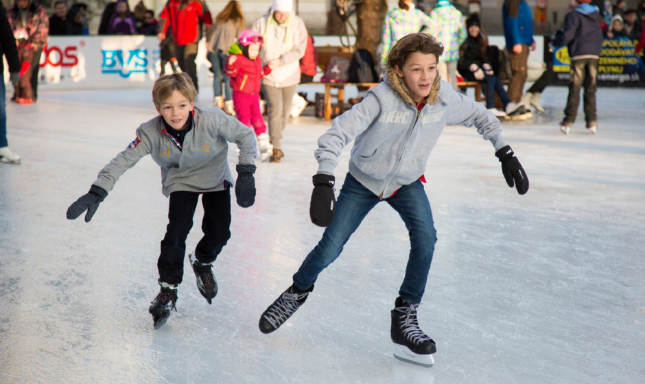 Photo of two boys one older and one younger skating and they appear to be racing each other. In the background there are other people a skating.