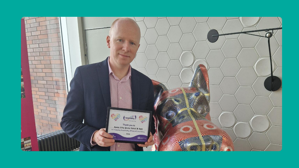 Paul Mooney - General Manager for Alex Hotel, Dundee poses next to Scotty Statue and is holding a certificate in recognition of providing respitality to unpaid carers