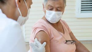 An older woman sits looking at her arm while she is getting a vaccination administered by a nurse/doctor