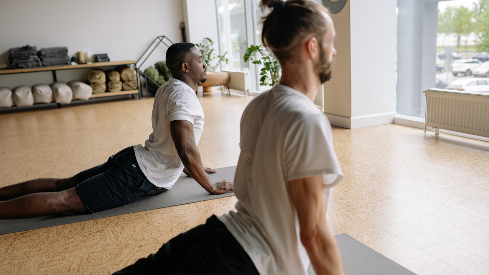 Two mens in a yoga studio. Both mens are on yoga mats doing an upward facing dog.