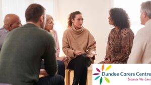 Mixed group of people gathered round on chairs having a discussion. Dundee Carers Centre logo is on the bottom right.