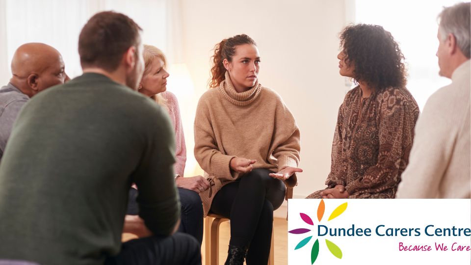 Mixed group of people gathered round on chairs having a discussion. Dundee Carers Centre logo is on the bottom right.