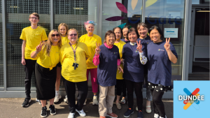 A group of people in yellow and blue t-shirts outside the C-Gate Centre. Kiltwalk Dundee logo is at the bottom right of the photo.