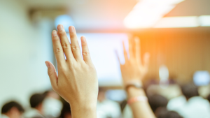 A picture showing the back of peoples heads that are blurred out . In the forground there are two hands up.