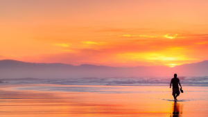 Image of a sunset at at beach and a silhouette of a person walking on the beach.